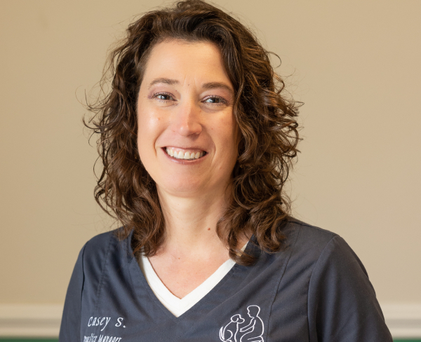 Woman with curly hair smiling in a navy blue medical uniform.