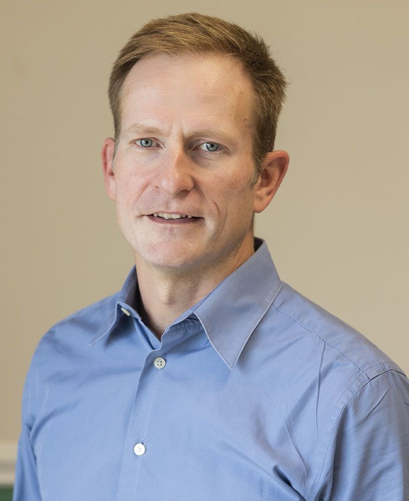 Middle-aged man with short hair, smiling, wearing a blue shirt.