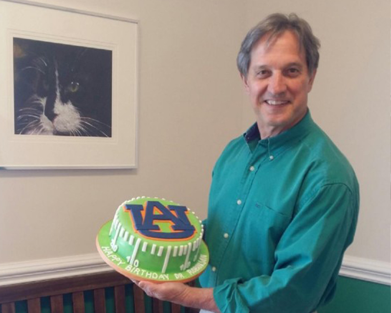Man holding a colorful birthday cake with "AI" design, next to a cat portrait.